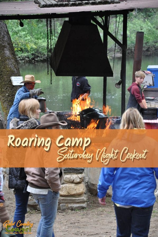 people standing around a roaring fire by the river with text overlay: Roaring Camp Saturday Night Cookout