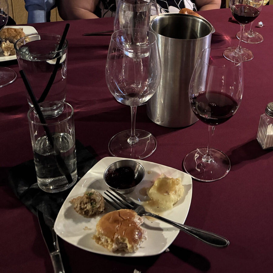 A small plate with a turkey slider, mashed potatoes, stuffing and cranberry sauce in front of two wine glasses for wine and food pairing tasting