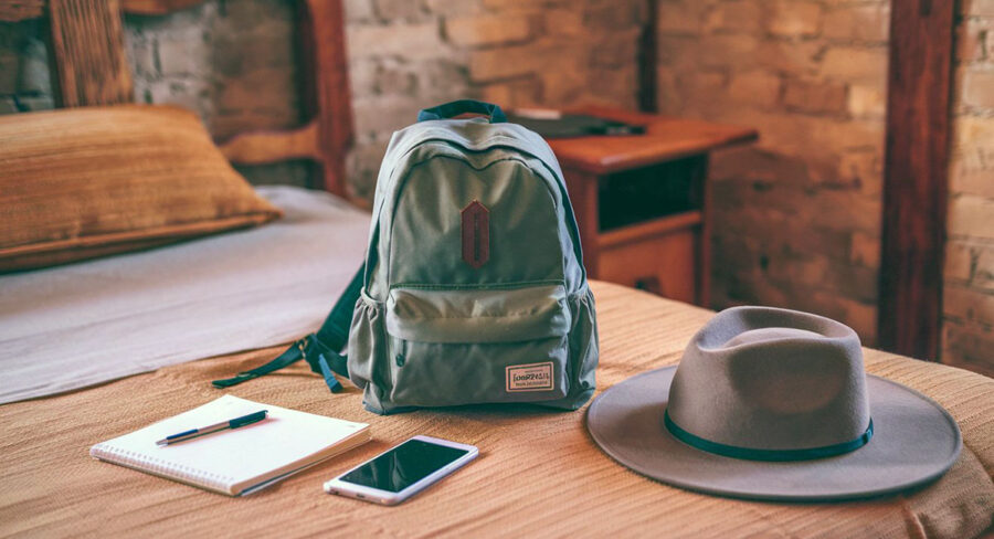 Back pack on a bed ready to be packed with some items suggested in the day trip packing guide: notepad and pen, cell phone and wide-brimmed hat.