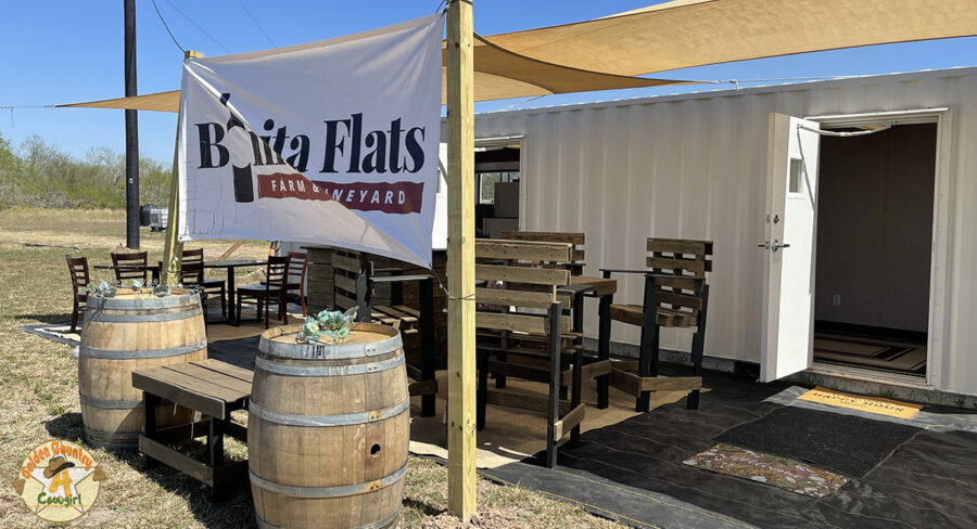 A white building with a canopy, table and chairs, and a banner with the winery name.